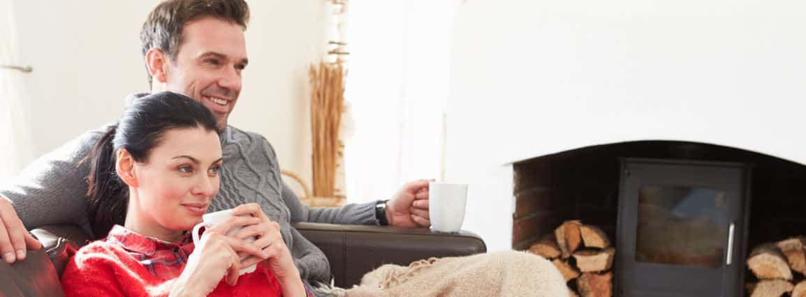 Couple relaxing on couch with blanket and coffee watching TV