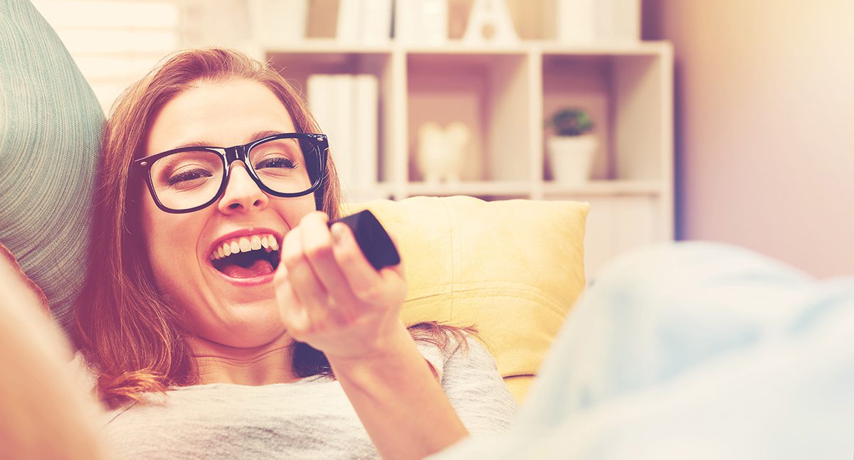 Young woman laughing and pointing remote at TV.
