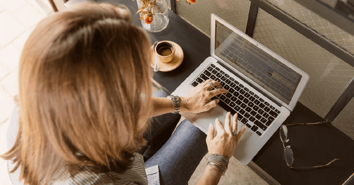 Woman using laptop with coffee and glasses nearby