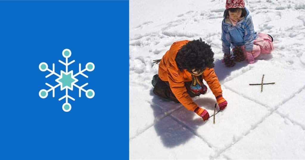 Young boy and young girl play tic-tac-toe with sticks and a pinecone on a board drawn in the snow.