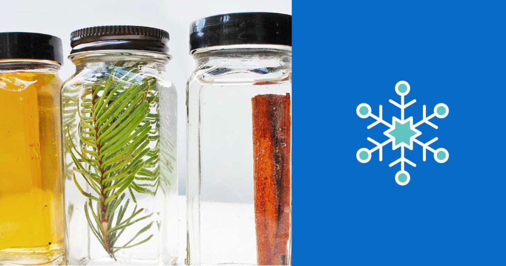 Three clear, rectangular, tall closed containers with liquid, pine branch pieces, and cinnamon sticks inside.