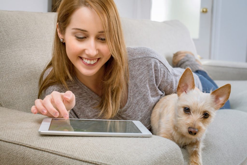 Woman on couch with dog and tablet.