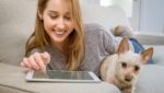 Woman on couch with dog and tablet.