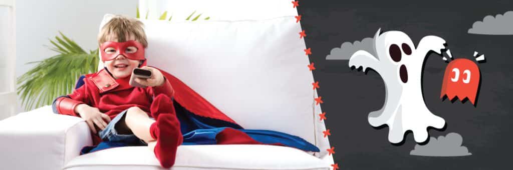 Boy in superman costume watching TV on white couch.