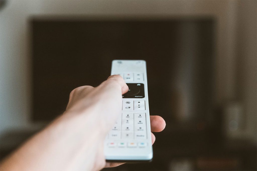 Hand on remote pointing to TV screen.