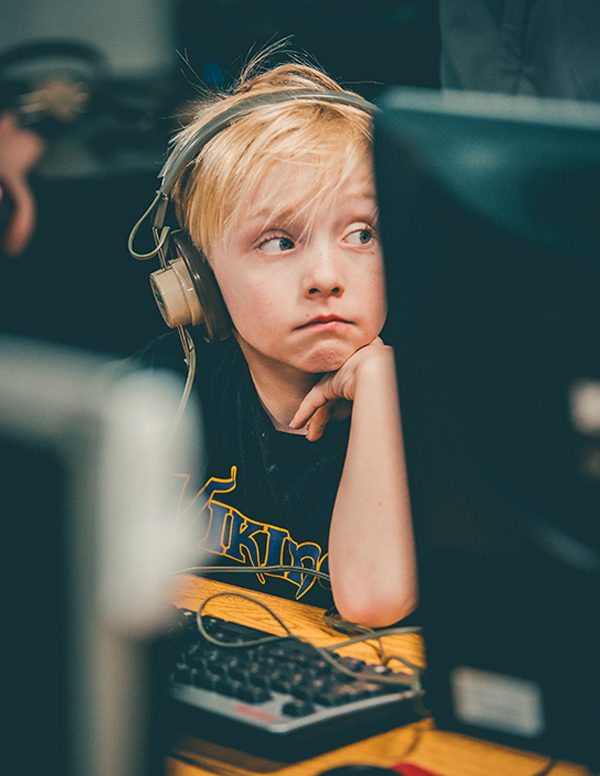 Young boy wearing headphones sits at desk in front of computer.
