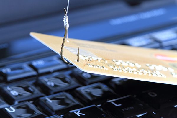Phishing scam depicted with a metal hook piercing credit card on top of keyboard.