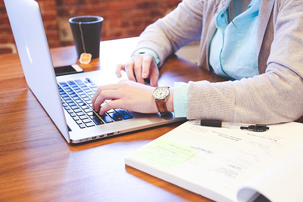 Woman’s using mac laptop computer with book open next to her and a cup of tea.