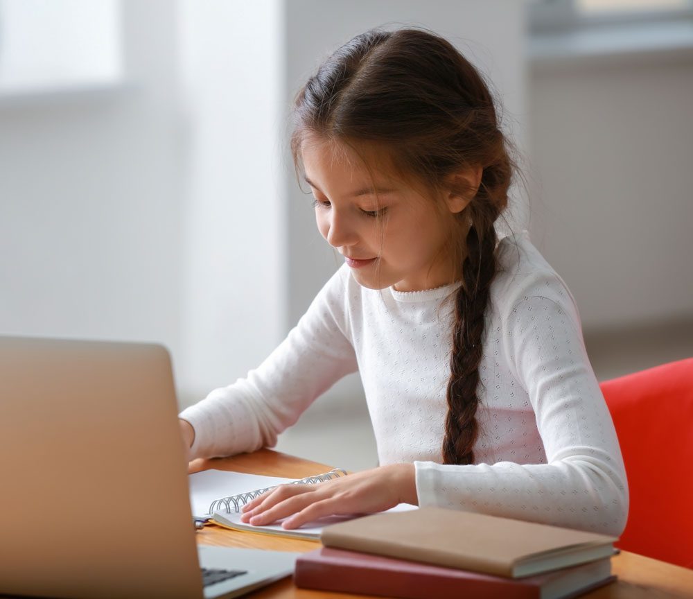 Young girl doing homework on desk with computer.