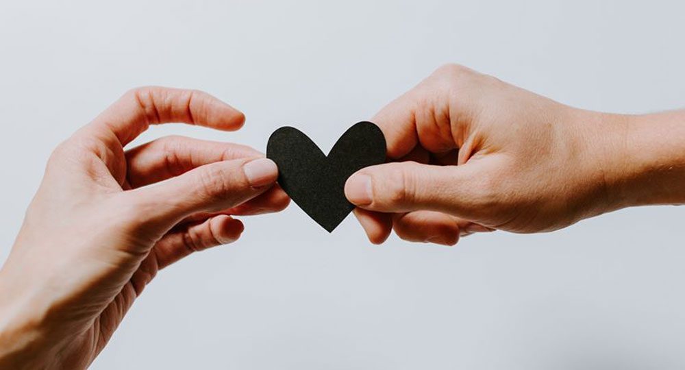 Hands holding a black paper heart.