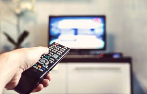Person pointing remote control at television.