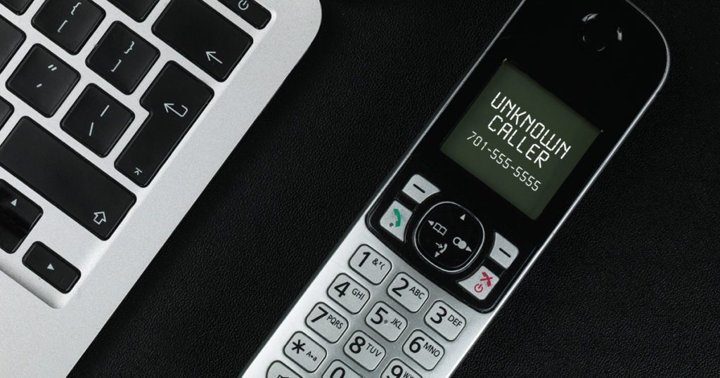 Telephone handset sits next to computer on desk.