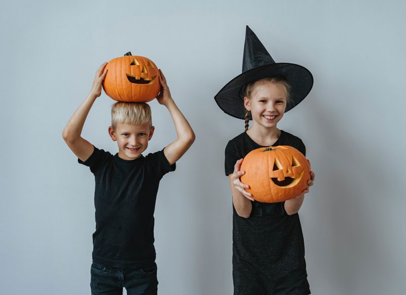 Two young kids holding jack-o-lanterns.