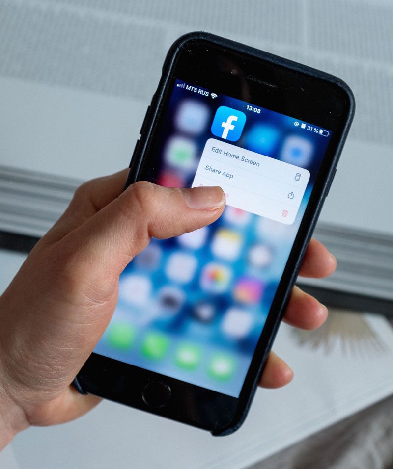 Close-up of person holding cellphone as they delete the Facebook app.