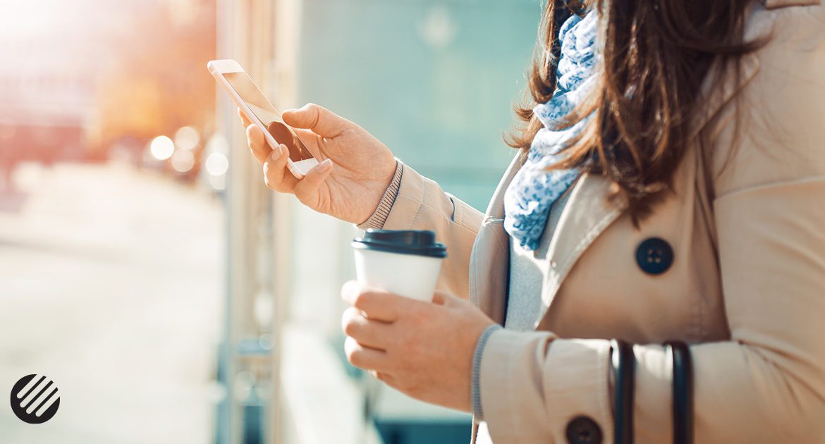 Woman holding cellphone and cup of coffee outside.