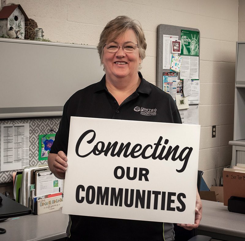 United Communications customer service representative Peggy Lider smiling and holding a sign that says “Connecting Our Communities”