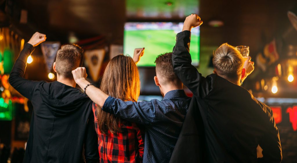 Young sports fans cheering for a game on TV at a sports bar