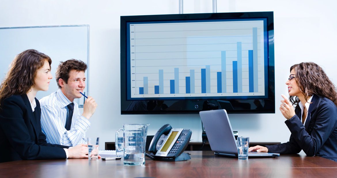 Two women and a man in a boardroom discussing analytics at a business meeting