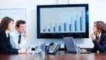Two women and a man in a boardroom discussing analytics at a business meeting
