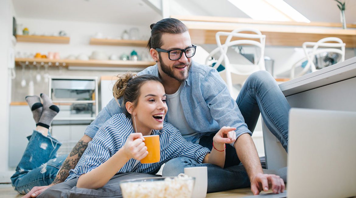 Young couple watching a movie on their laptop on the kitchen floor.