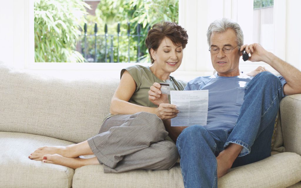 Middle-aged couple looking at a phone bill and talking on the phone.