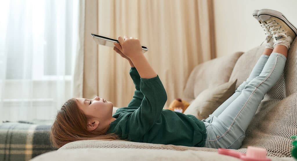 Young girl laying on couch using tablet.