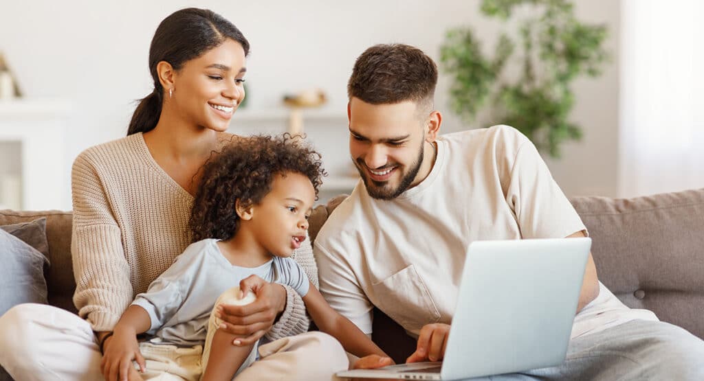 Two parents and child using laptop together.