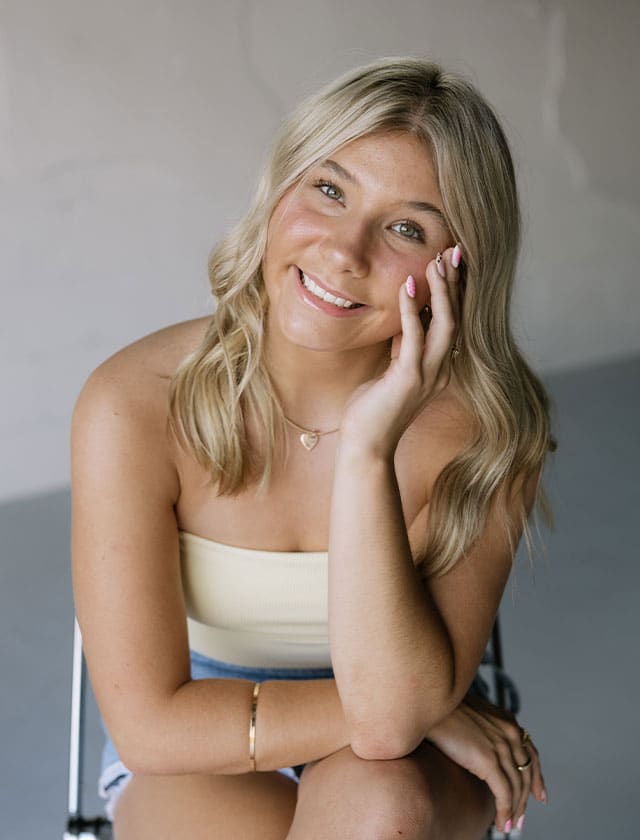 Smiling blonde woman resting her head on her hand, looking at the camera.
