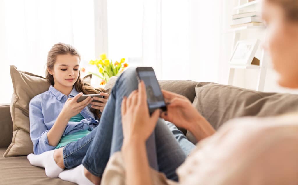 Two teenage girls watching videos on their cell phones while sitting on the couch