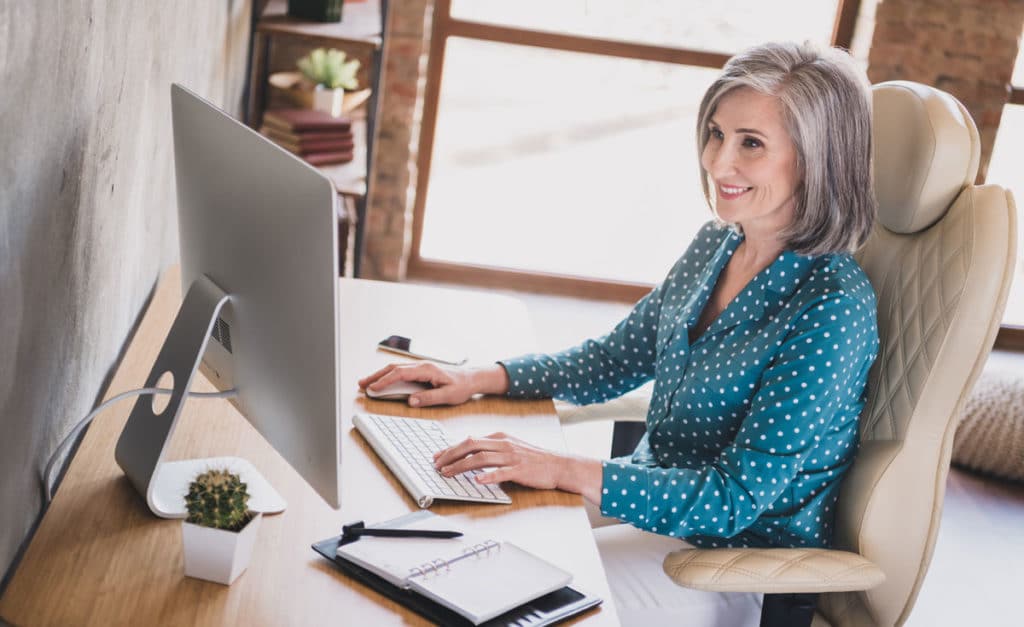 A middle-aged woman working in a modern office on a desktop computer